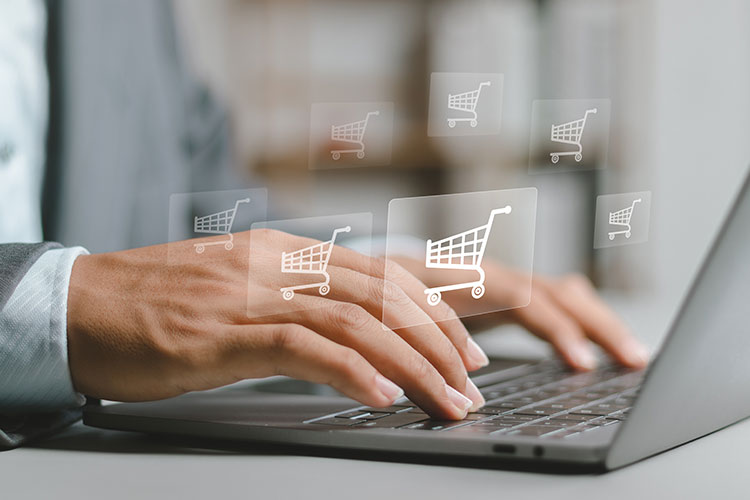Hands tap on laptop with shopping cart icons.